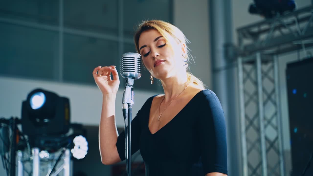 Musical star on the stage. Attractive woman singer performing a live music into the microphone for special event. Slow motion.