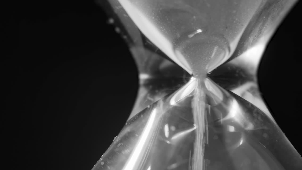 Sand of hourglass falling through narrow bottleneck, telephoto closeup
