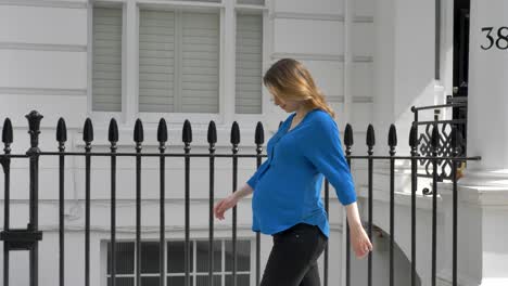 heavily pregnant caucasian woman walking down beautiful white stucco street in london