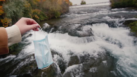 a man holds a medical mask against the backdrop of a clear mountain river. the end of quarantine and disease concept