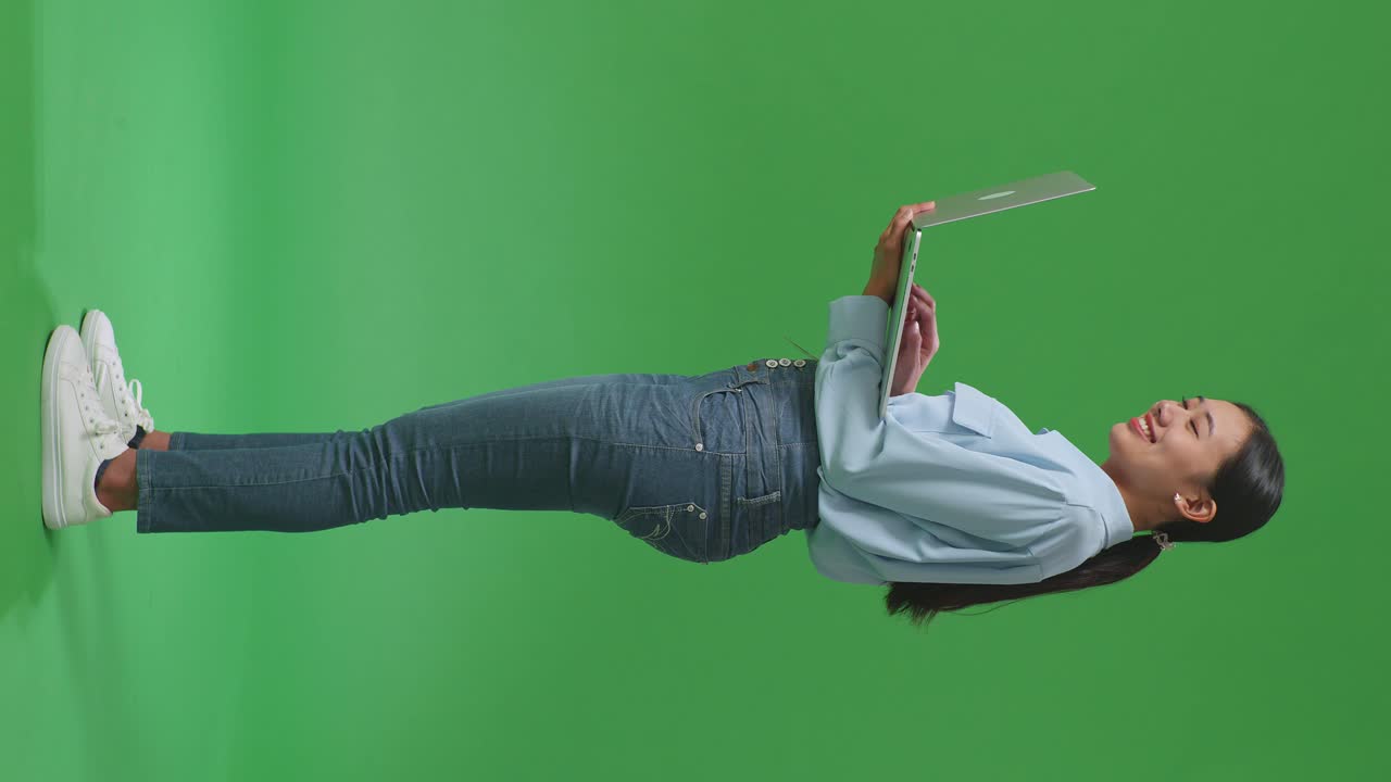 vista lateral de cuerpo completo mujer de negocios asiática usando computadora portátil en fondo de pantalla verde en el estudio