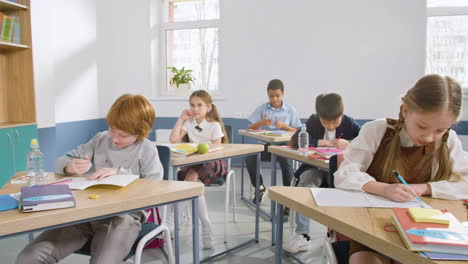 multi-etnische groep studenten die aan een bureau in een engels klaslokaal zitten en in hun notitieboekjes schrijven