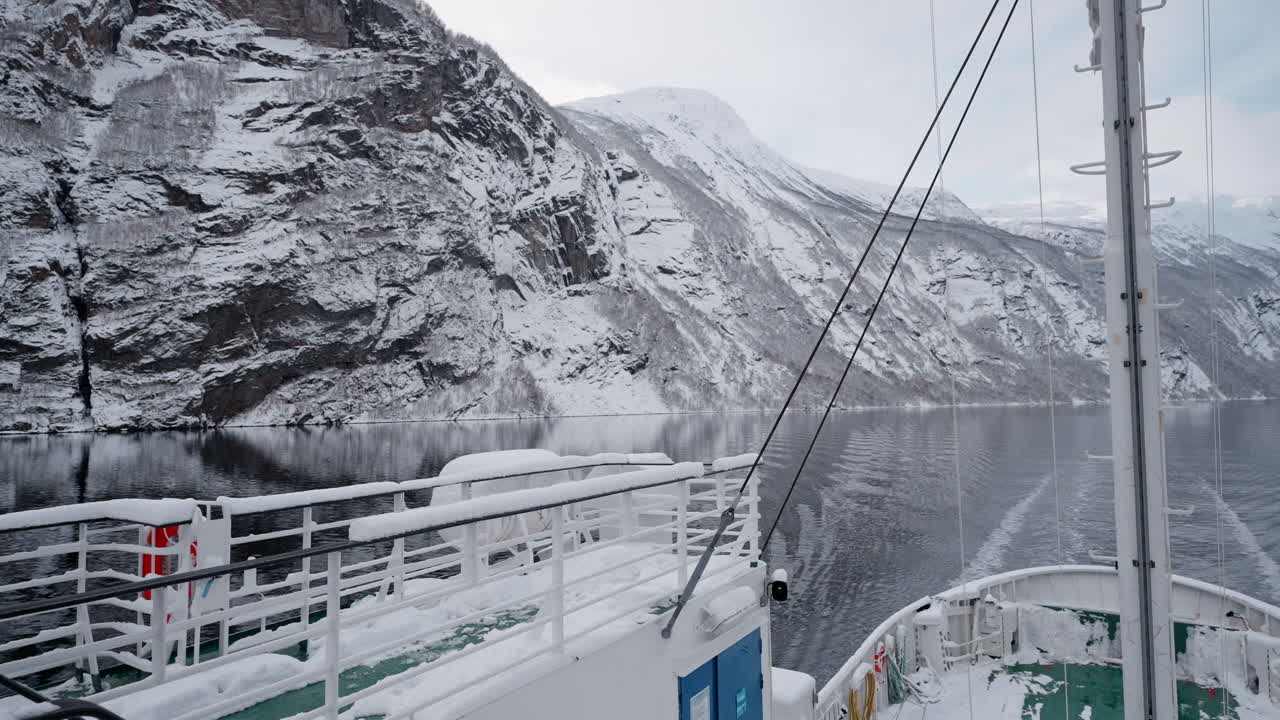 vídeo de un viaje en ferry a través de geirangerfjord en invierno, con impresionantes vistas de montañas cubiertas de nieve, un cielo brillante y reflejos en el fiordo