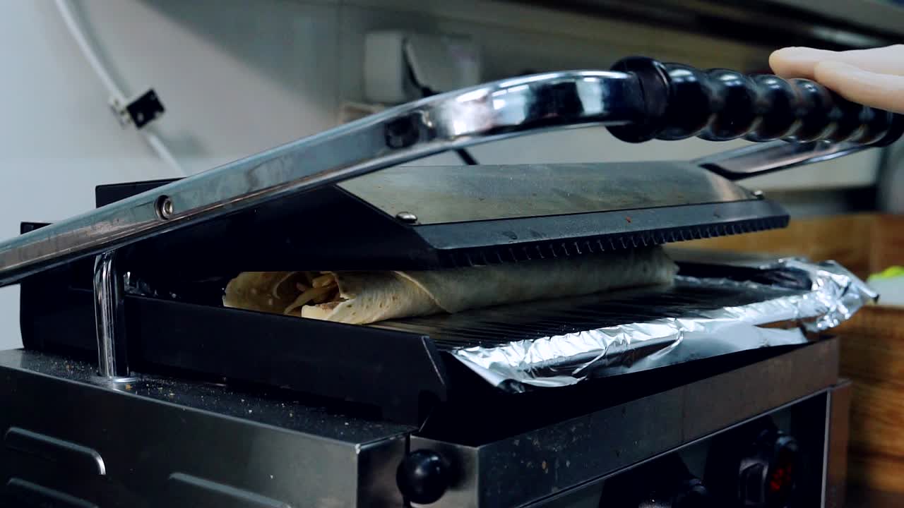 Chef puts pita into grill machine. Roll of pita bread frying in fast food restaurant. Cooking delicious snack