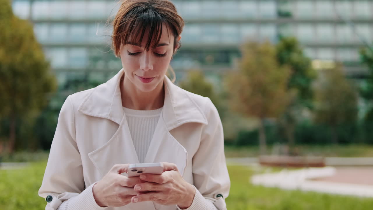 Giovane donna che messaggia con lo smartphone in un parco urbano