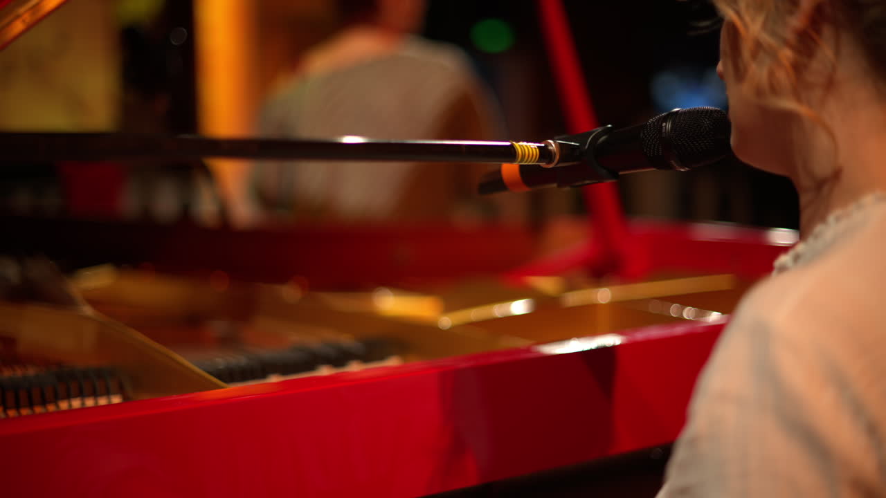 Woman singing into the microphone and playing a red piano
