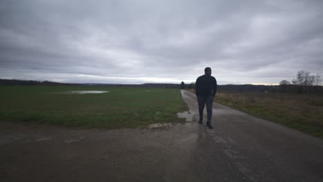 modern black male waiting in open field under grey sky, europe, 4k | muscular, intimidating, shadow, figure, blurry, dark clothes, powerful, walk towards, distant, thought, thinking