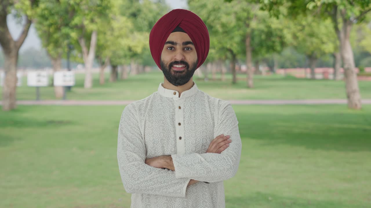 hombre indio sikh feliz de pie con las manos cruzadas en el parque