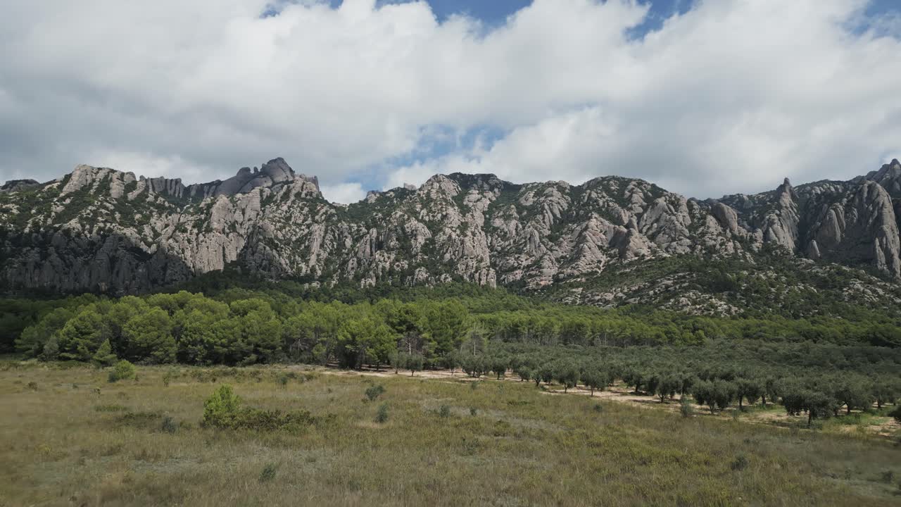Spectacular aerial drone view flying towards the unique rock formations of montserrat mountain, a multi peaked range in catalonia, spain, featuring lush green forests and a partly cloudy sky