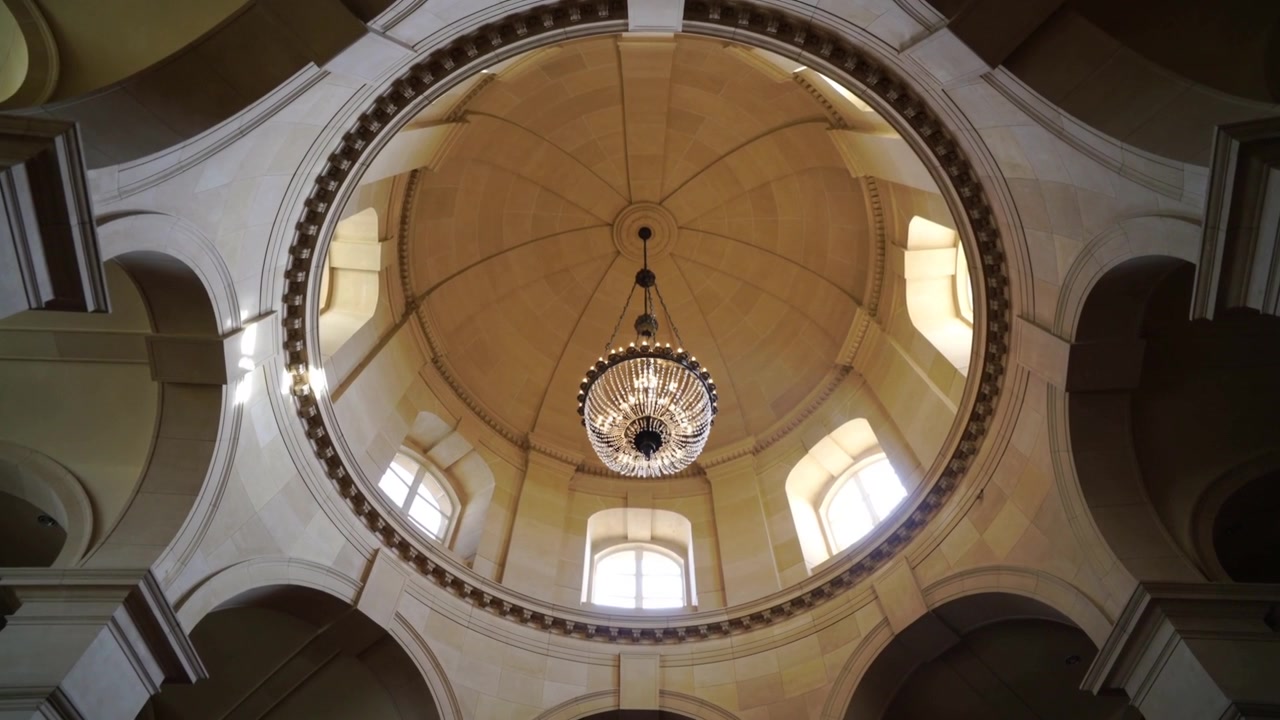 Iniciando inclinación, la cámara estabilizándose, reencuadrando para centrar la araña de luces en la cúpula de la capilla, brillando