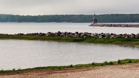 an old chapel stands on a stone promontory on the water in leningrad region russia at cloudy weather, the forest in the background