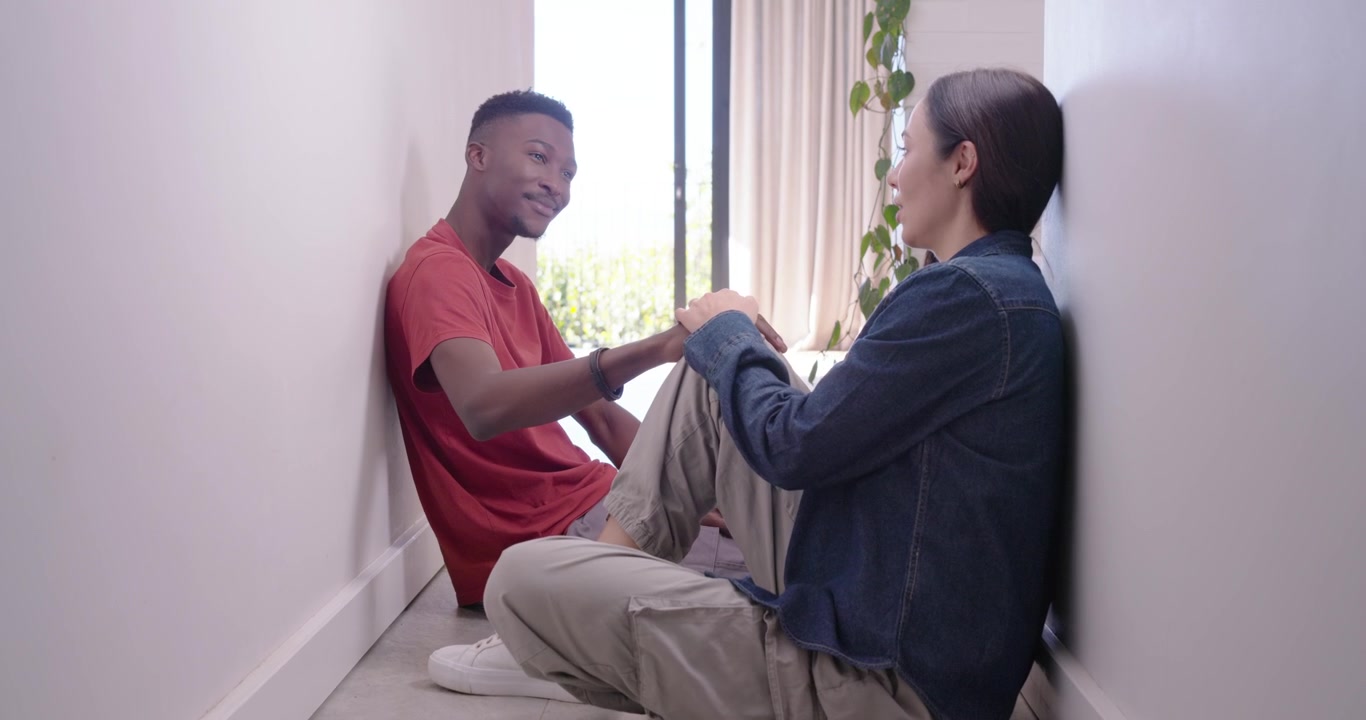 Couple sitting on hallway floor, man in red T-shirt starting talk, touching woman's knee comforting
