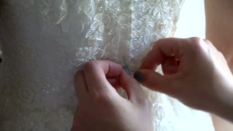 Close-up-of-bride-getting-help-getting-dressed-by-bridesmaid,-pulling-up-and-closing-buttons-at-brides-back-on-her-wedding-dress