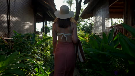 rear tracking shot of female tourist in swimwear walking towards resort pool