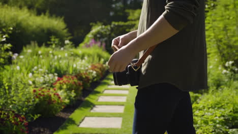 a person holding a camera walks along a path in a lush garden