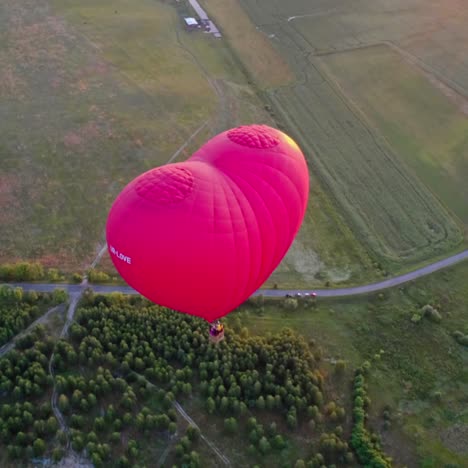 red aerostat over fields. romantic hot air balloon in a form of a heart travels in the sky on beautiful nature background at sunset. top aerial view.