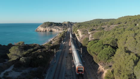 drone flying over cliff as train passes underneath towards rocky sea coast