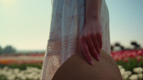 Closeup-unrecognizable-gentle-woman-in-dress-holding-straw-hat-in-tulip-field.