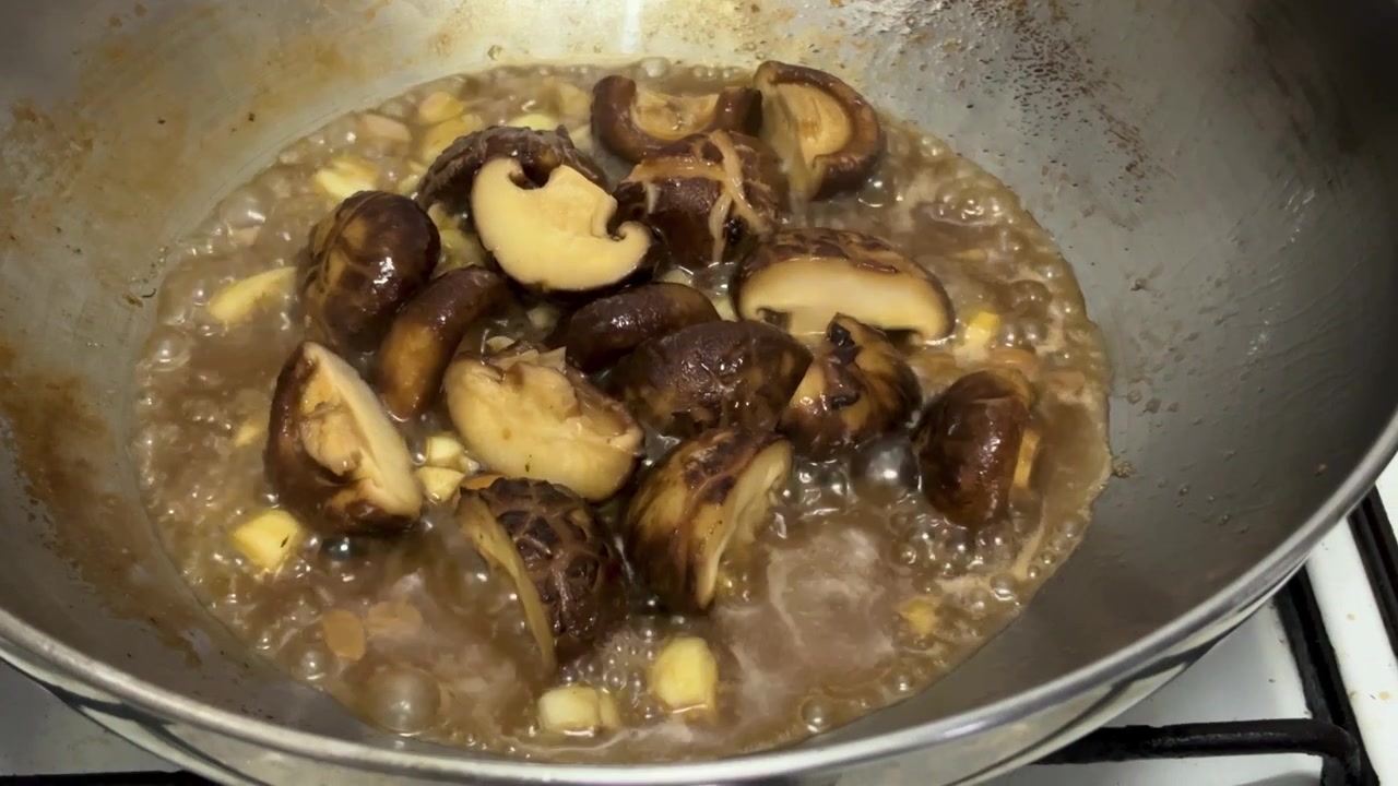 Statisk nærbilde tatt fra høy vinkel som fanger en velsmakende asiatisk rett under tilberedning. Rammen viser tykke halvdeler av shiitake-sopp som putrer og wokkes i en fyldig, brun østerssaus.