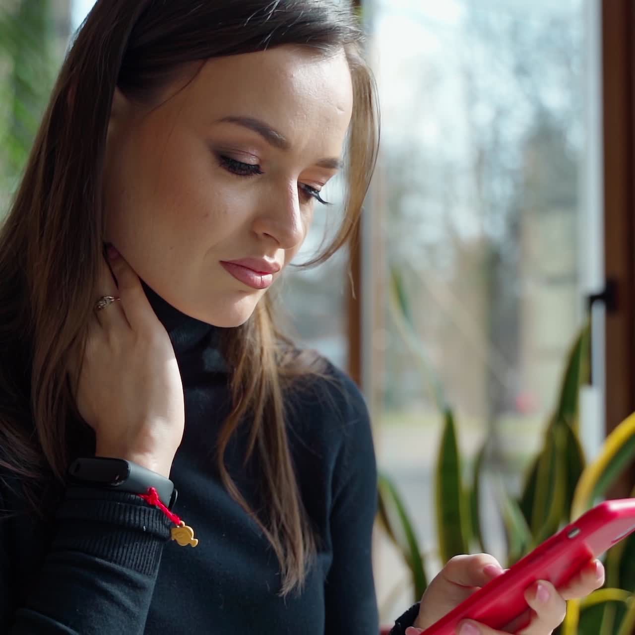 Side view of a lovely woman with a phone indoors. Young beautiful girl sitting in a cafe and looking into her mobile phone.