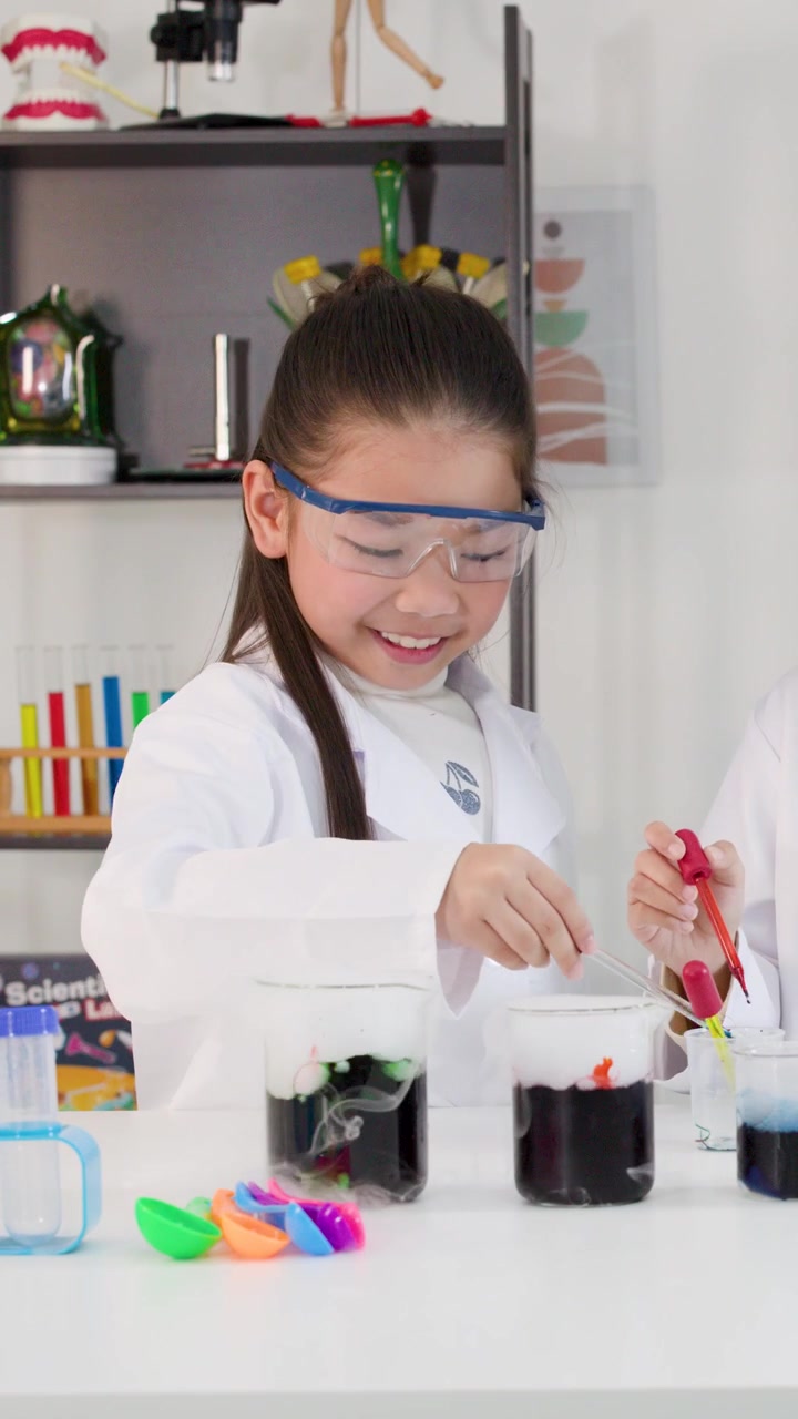 A young Asian girl wearing safety goggles uses droppers to conduct colorful science experiments