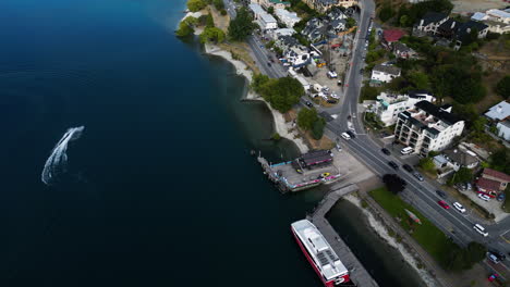 Aerial-tilt-up-view-of-boat-sailing-in-the-banks-of-a-big-lake-in-Queenstown,-New-Zealand