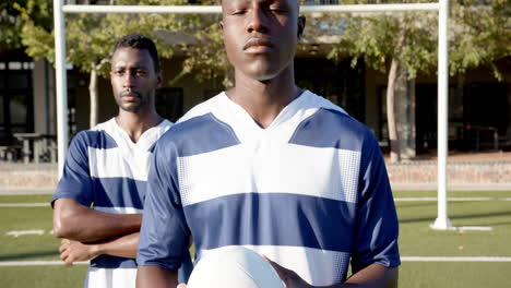 holding rugby ball, two african american male athletes in sports uniforms standing on field