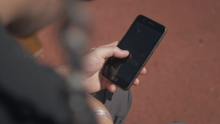 Giovane che naviga sui social media al telefono in un parco giochi d'estate