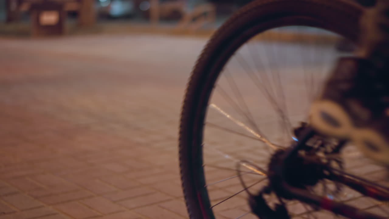 Close view of cyclists riding on a city street at night capturing the motion with a focus on the cyclists' wheels and the illuminated pavement
