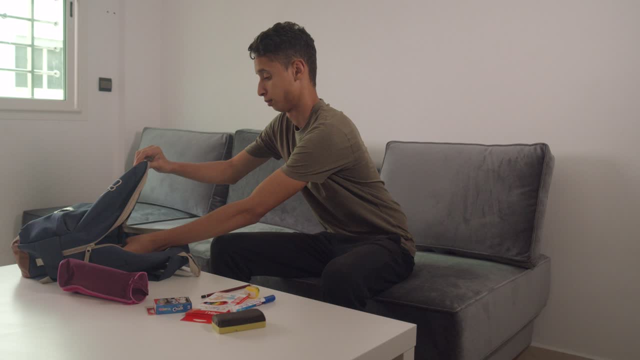 Teen Put His Things On His Backpack On Center Table Of Living Room