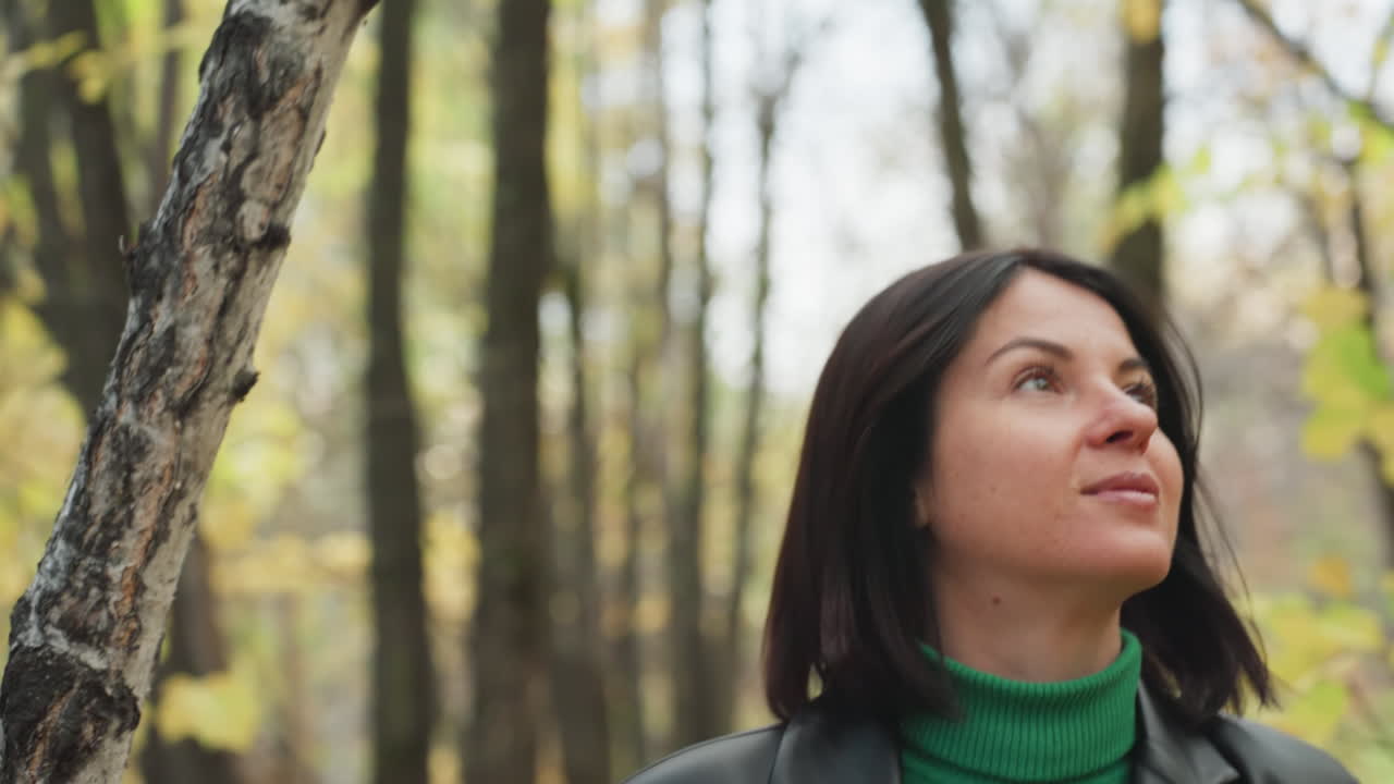 retrato de una mujer blanca en un bosque, miradas secuenciales hacia un lado y hacia arriba, expresión esperanzadora y sonrisa amable, jersey de cuello alto verde y chaqueta de cuero, luz solar moteada a través del dosel, introspectiva