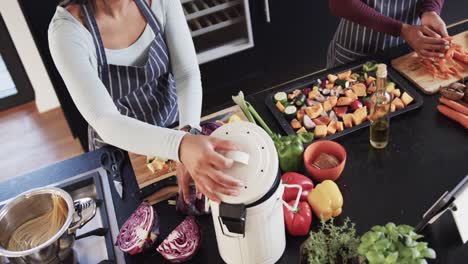 high angle of biracial lesbian couple in aprons composting vegetable waste in kitchen, slow motion