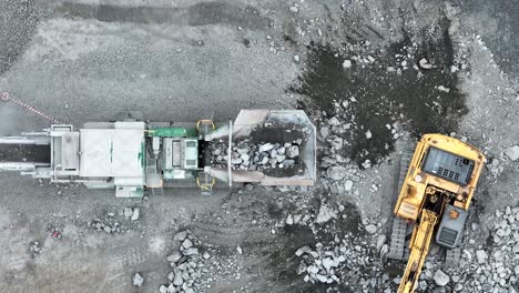 aerial top down shot of excavator placing rocks into conveyor belt sorting machine