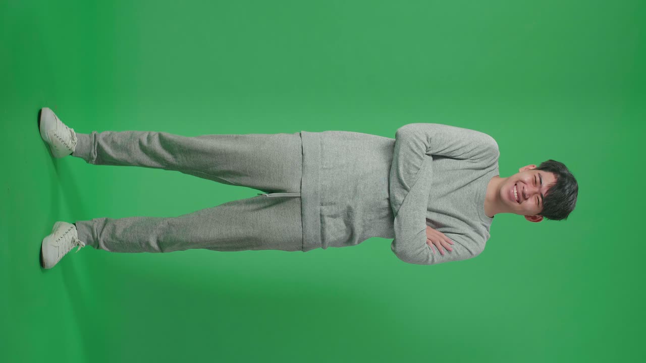 Full Body Of Smiling Asian Man Crossing Her Arms While Standing In Front Of Green Screen Background