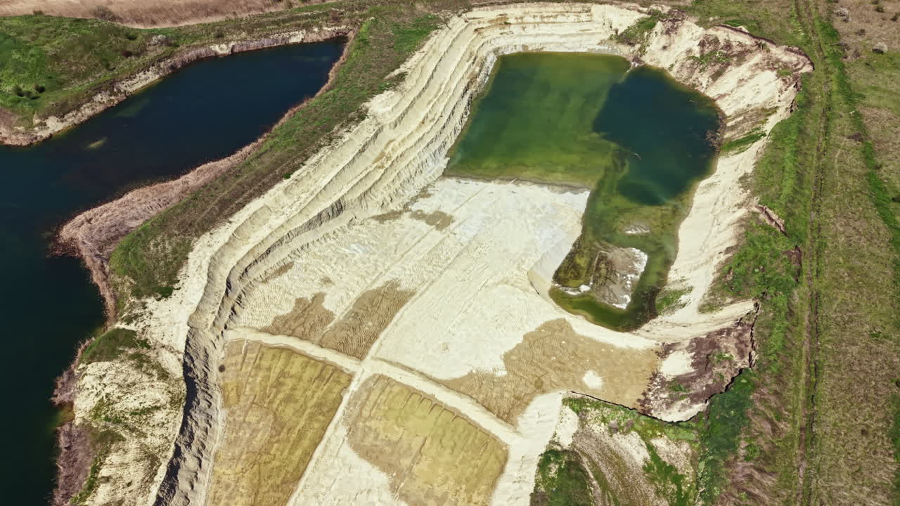 Large sand quarry with water pools showing layers of earth and mining activity during daylight