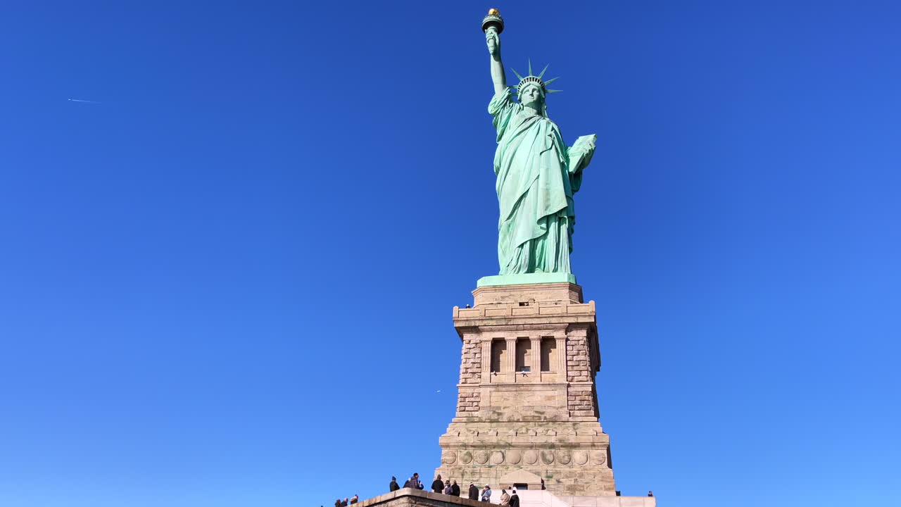 Tourists enjoy the view of the tall Statue of Liberty in New York City on a sunny day