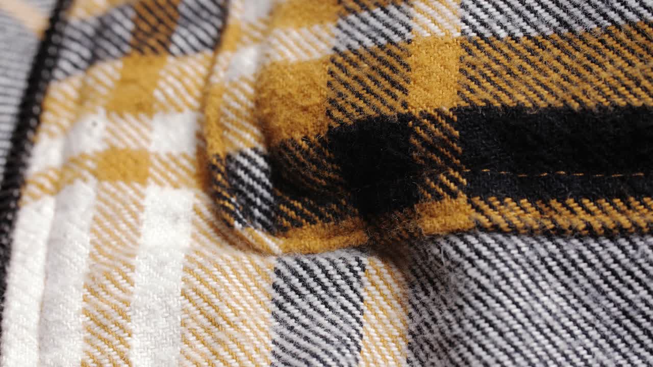 Mustard plaid flannel shows its brushed texture and zipper teeth as the camera pans slowly left to right