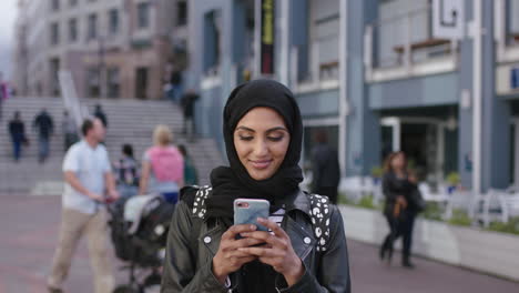 retrato de una joven mujer de oriente medio mirando un teléfono inteligente sorprendida emocionada en el fondo urbano