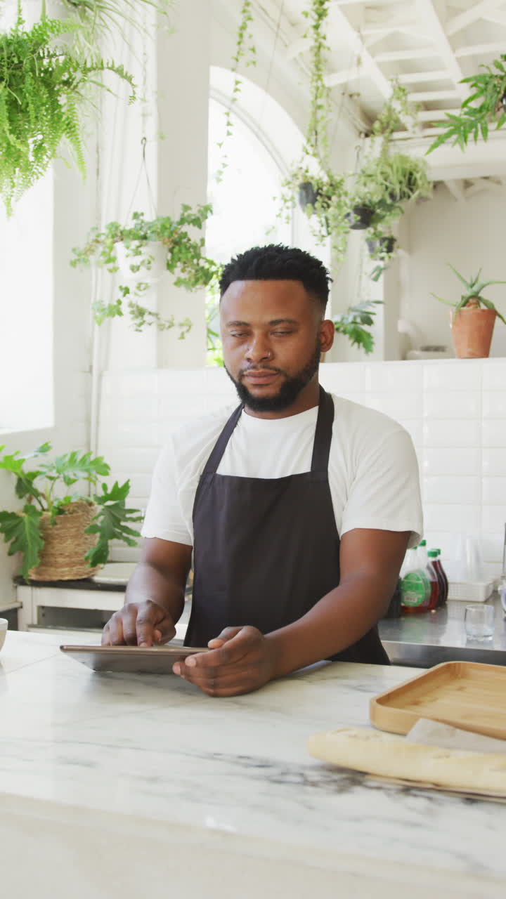 video vertical del retrato de un barista afroamericano sonriendo y usando una tableta en un café