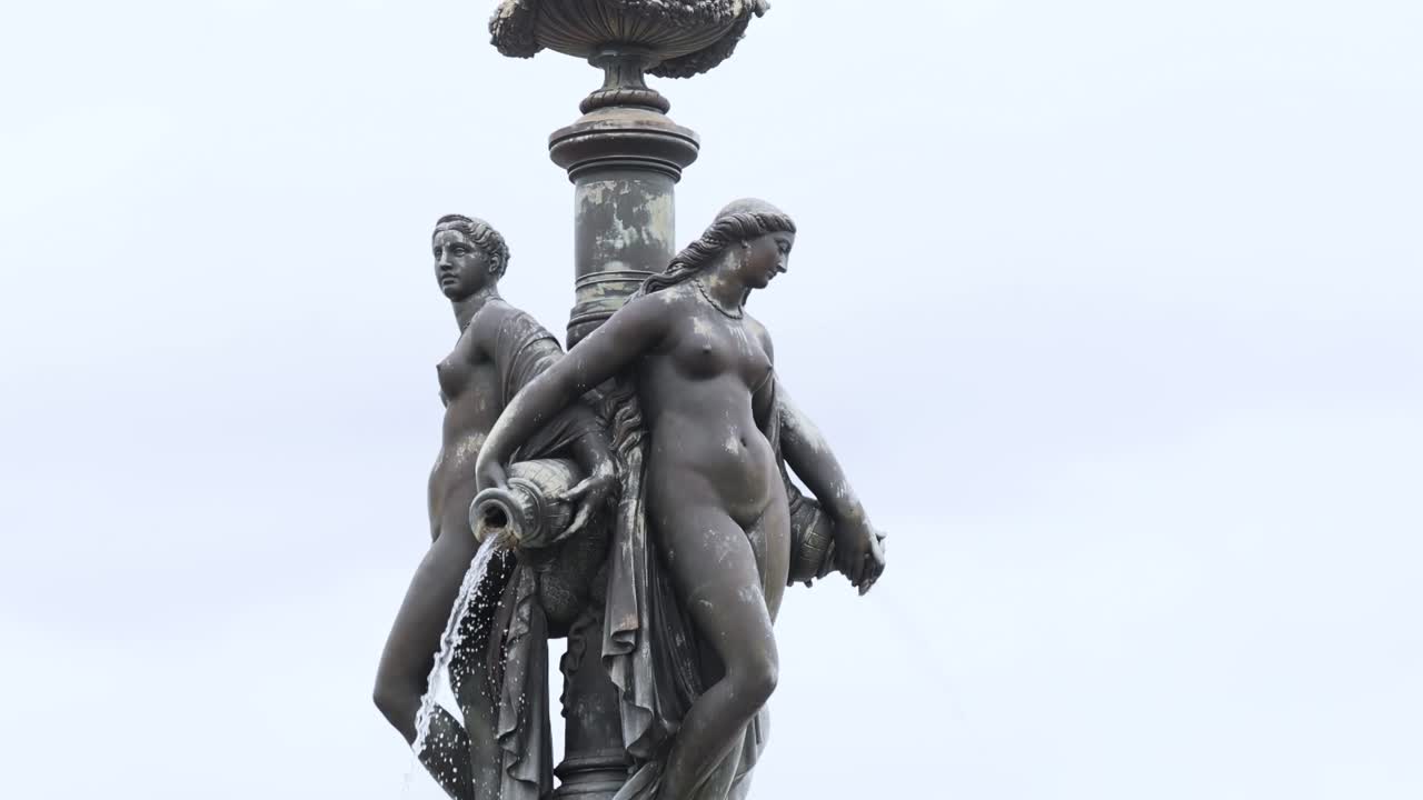 Detailed view of two bronze figures atop a decorative pedestal against a clear sky.