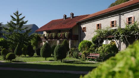 Moraca (Morača) Monastery stone building facade with red tiled roof, wooden shutters, balcony flowers, and manicured trees, Montenegro