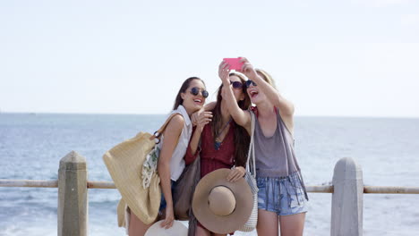 tres mujeres jóvenes en vacaciones de verano tomando selfies en el paseo marítimo de la playa con pantalones cortos de mezclilla