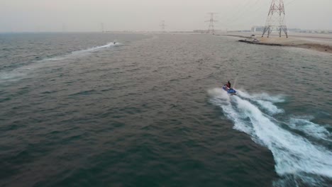 high octane drone chases jet ski's as they fly across water next to coastline and electrical pylons