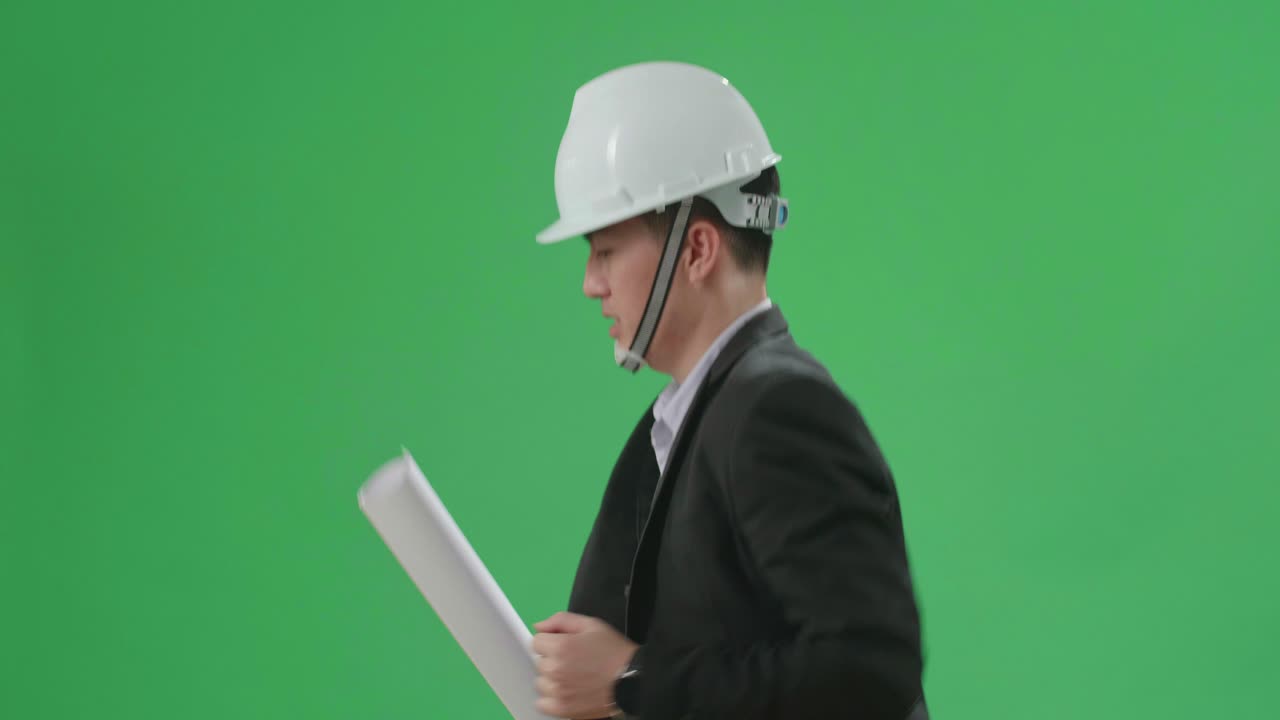 Side View Of Asian Chief Engineer In The Hard Hat Holding Blueprint And Runs On Green Screen Chroma Key