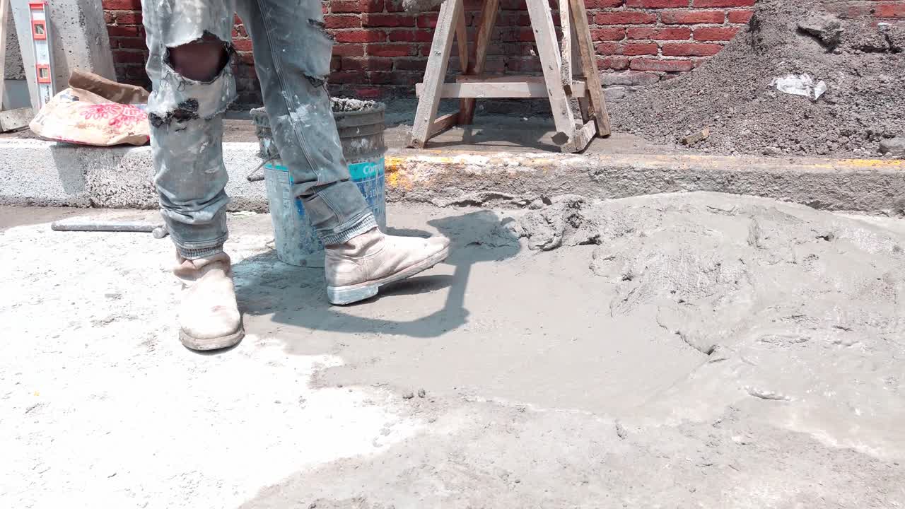 Worker pouring fresh cement onto pavement at a sunny outdoor construction site