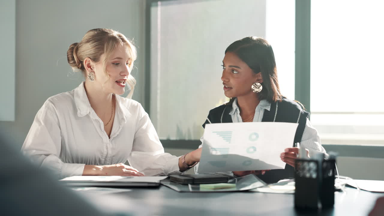 Two businesswomen collaborating in an office meeting, reviewing charts and data