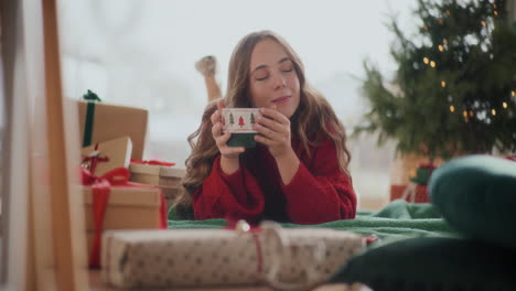 Mujer-Relajada-Sosteniendo-Una-Taza-De-Café-Mientras-Yacía-En-El-Suelo-Durante-La-Navidad