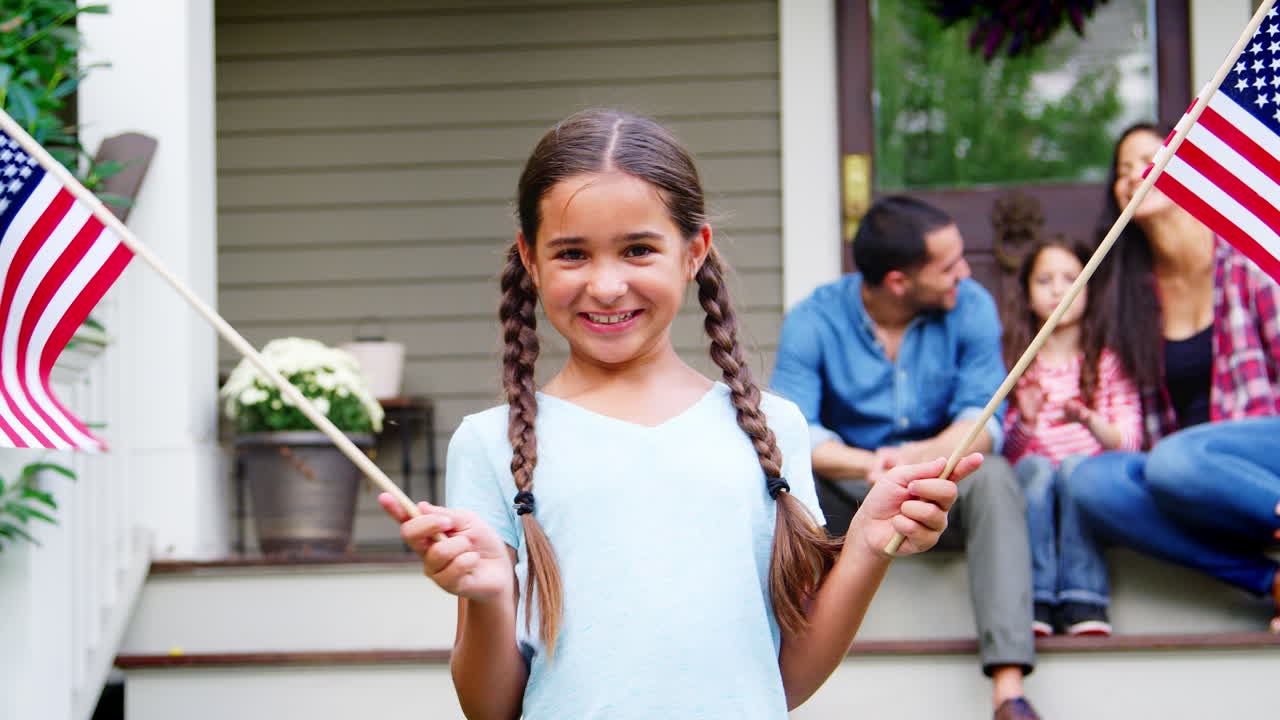 niña con familia fuera de la casa sosteniendo banderas estadounidenses