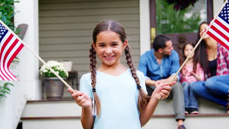 niña con familia fuera de la casa sosteniendo banderas estadounidenses