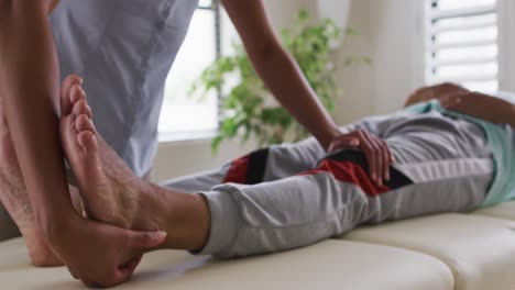 mixed race female physiotherapist helping senior man stretching his legs